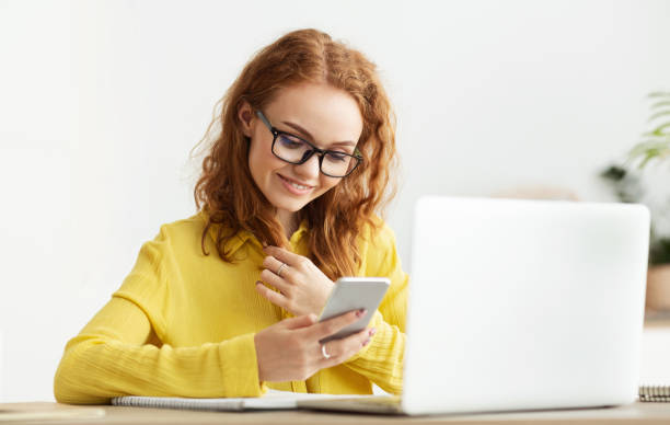 istock Young Woman in Yellow Shirt Smiles While Using Smartphone in Modern Workspace 2194292545
