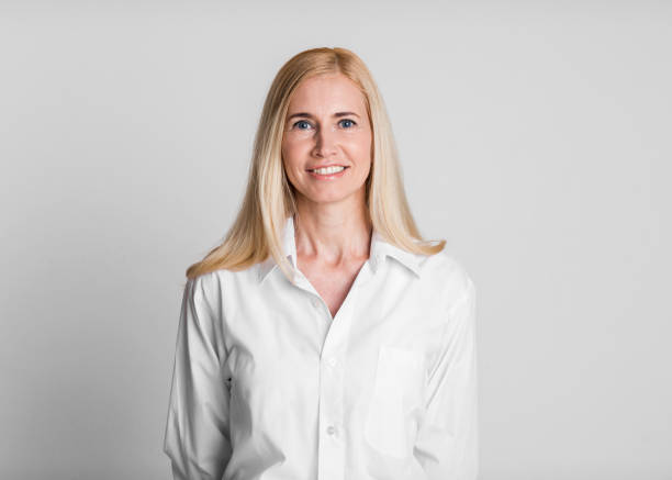 Smiling Woman in a White Shirt Posing Against a Light Gray Background in a Studio Setting