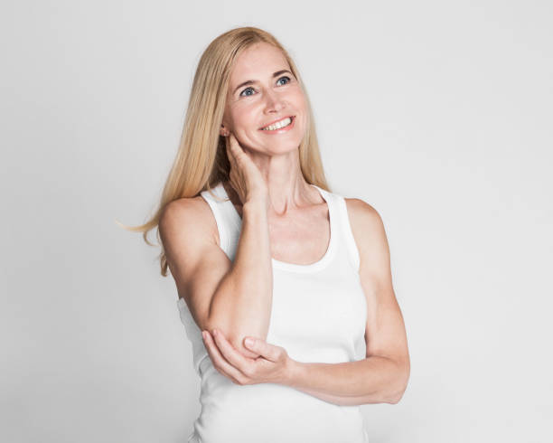 Woman in White Tank Top Smiling While Thinking Against a Light Gray Background