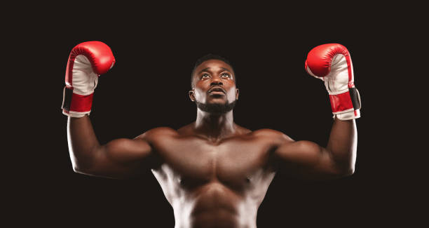 istock Strong Boxer Celebrating Victory With Raised Gloves in the Spotlight 2194294053