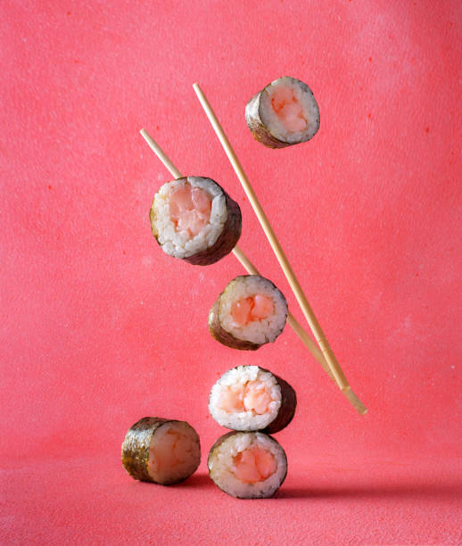 istock Classic sushi rolls with chopsticks falling down on a pink background. Sushi rolls levitate in the air 2194298958