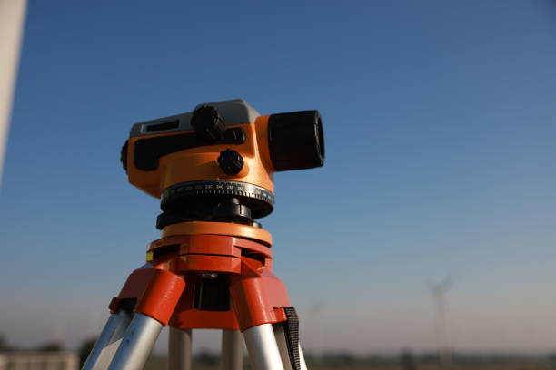 A young engineer is looking through a survey camera to level the area for road construction in a wind power generating area.