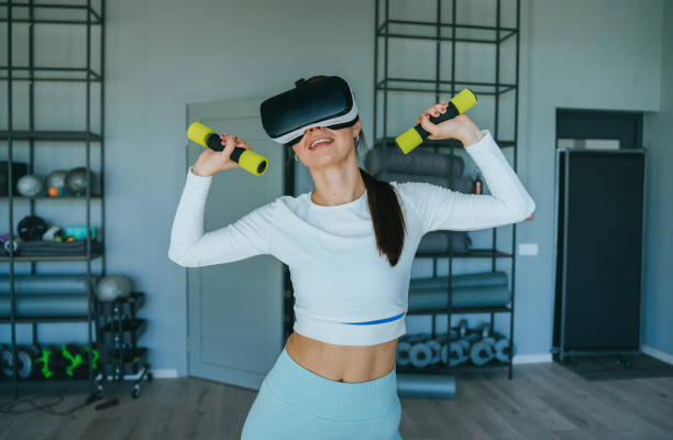 istock Slim brunette hispanic girl in sportswear training with dumbbells using virtual reality headset at sport club. Active young American woman lifting up dumbbells against shelves with sport gear. 2194302749