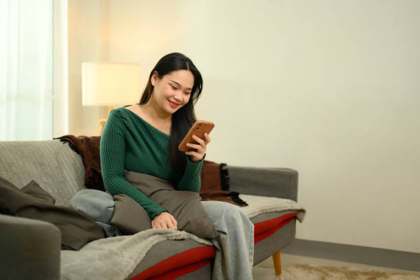 istock Pretty young woman in green sweater using her mobile phone on a cozy sofa 2194311939