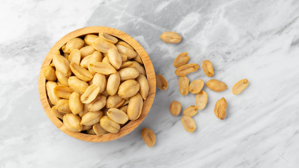 istock Salted roasted peanuts in wooden bowl on marble table, top view 2194312006