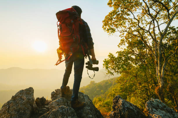 istock man with a backpack is standing on a mountain top, looking out at the sunset 2194319262