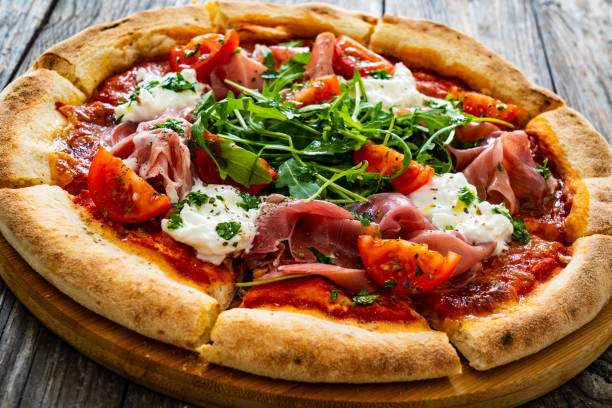 istock Pizza prosciutto - cured ham, white mushrooms, arugula and cheese on wooden table 2194322762