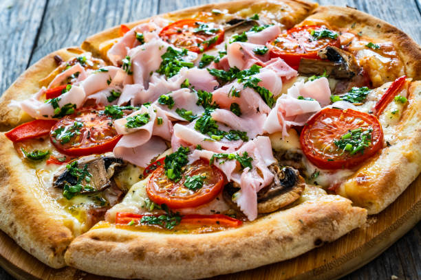 istock Pizza with ham, mozzarella cheese, sliced tomatoes and white mushrooms on wooden table 2194323145