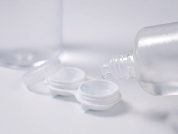 istock Transparent liquid dripping into an open contact lens case from a plastic solution bottle on a white background. Concept of lens care, hygiene, and eye health 2194325476