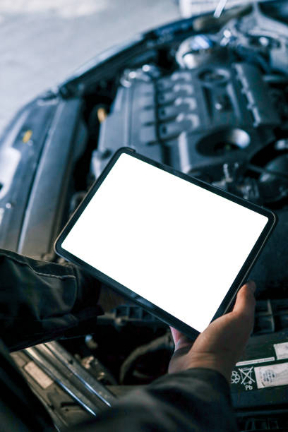 istock A tablet with a blank screen held by a mechanic above a car engine, symbolizing modern diagnostic tools for vehicle maintenance and repair. The engine is visible in the background 2194327372