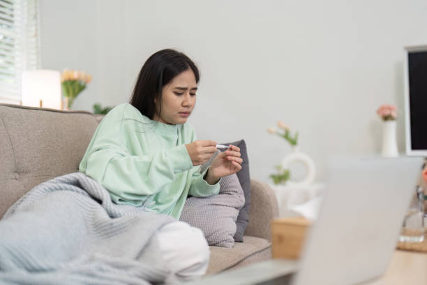 istock Woman Checking Temperature at Home While Feeling Unwell, Wrapped in Blanket on Sofa, Illustrating Healthcare and Sickness 2194344986