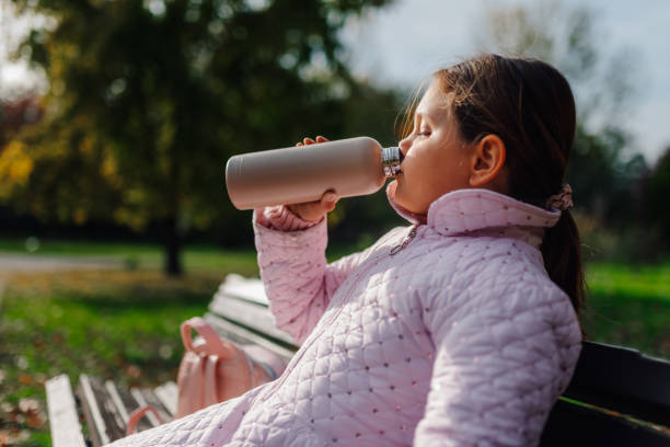 istock Young girl drinking from reusable water bottle in a park 2194345207
