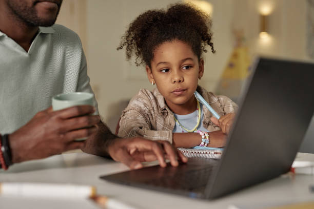 istock Black Girl Watching Dad Using Laptop while Working on Homework Together at Home 2194353334