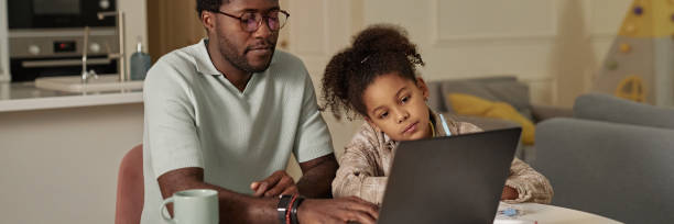 istock Header Image of Black Man Typing on Laptop Teaching Daughter how to Use Computer at Home 2194353408