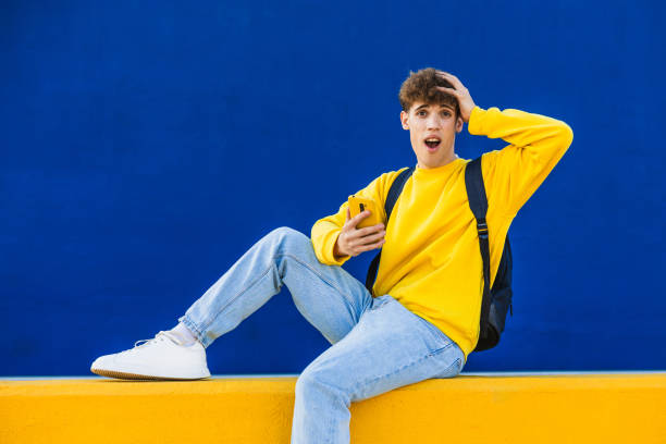 istock Shocked college student looking at smartphone sitting on yellow bench 2194354744