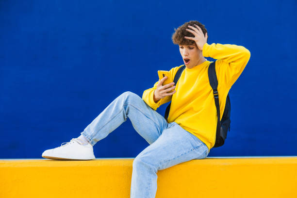 istock Shocked college student looking at smartphone sitting on yellow wall 2194354752