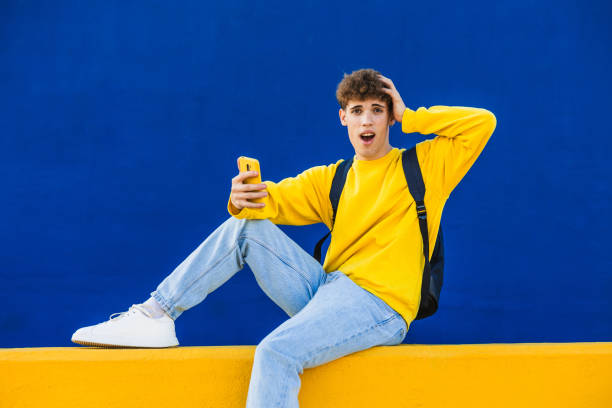 istock Shocked college student looking at smartphone while sitting on yellow ledge 2194354768