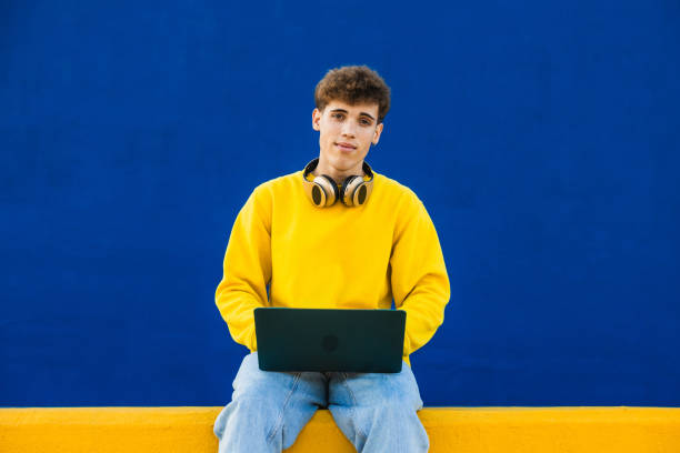 istock Young man using laptop with headphones around neck on colorful background 2194355204