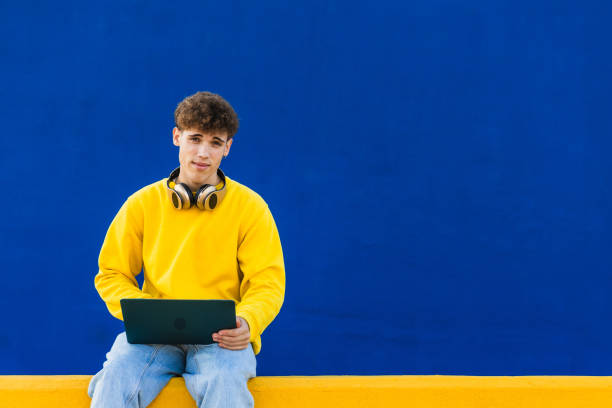 istock Young man using laptop with headphones around neck on colorful background 2194355211