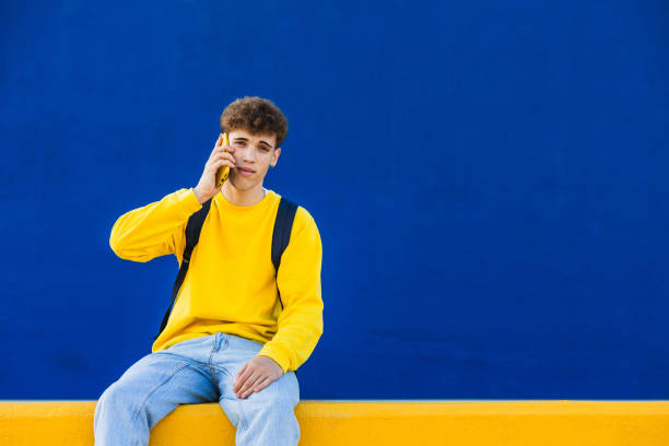 istock Young man with backpack talking on smartphone in front of blue wall 2194355266