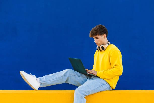 istock Young student working on laptop with headphones in vibrant urban setting 2194355518