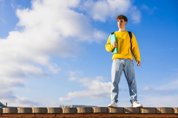 istock College student standing on a wall holding books and looking away 2194355535