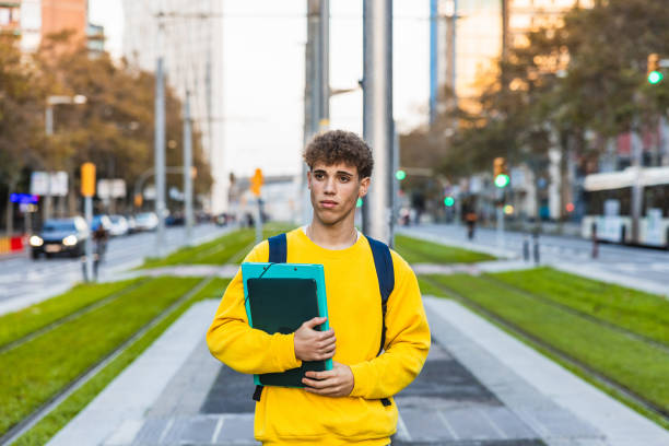 istock College student waiting at tram stop holding books and backpack 2194355701