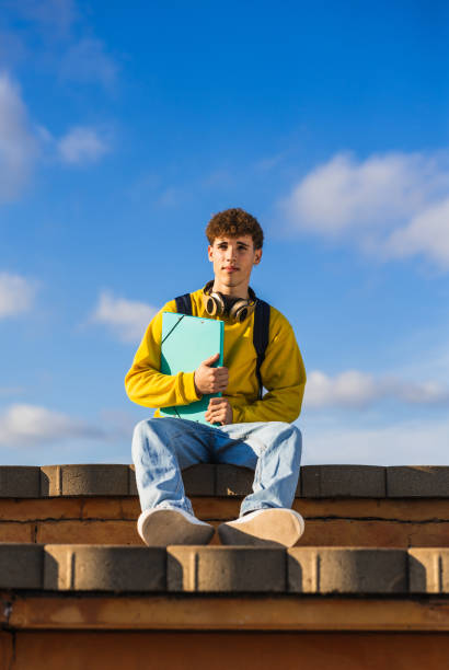 istock Young college student sitting on a roof holding a binder 2194356321