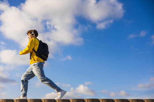 istock Young student walking on a wall with headphones and backpack 2194356740