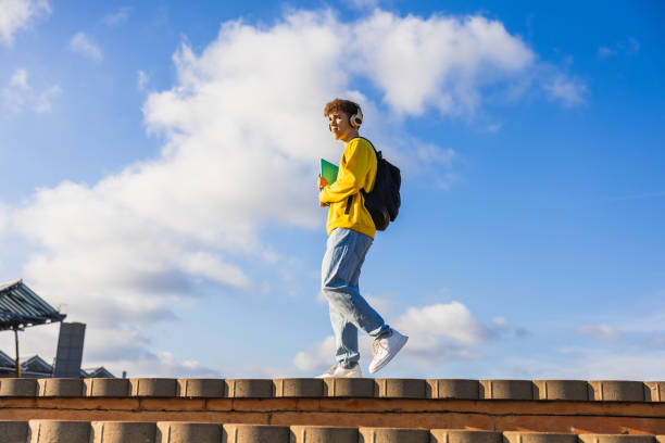 istock Young student walking with headphones and backpack on campus rooftop 2194356758