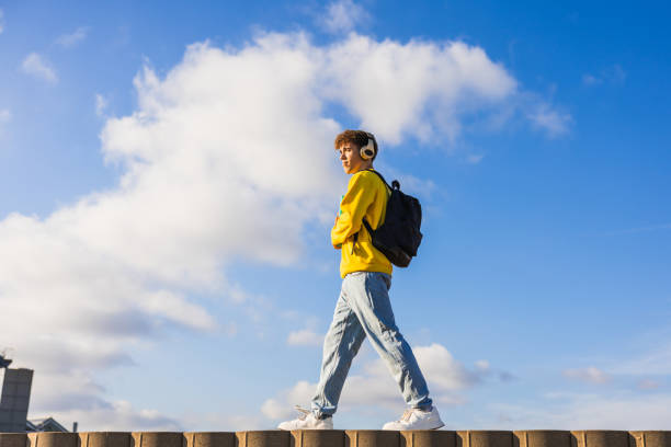 Young student walking with headphones and backpack under blue sky