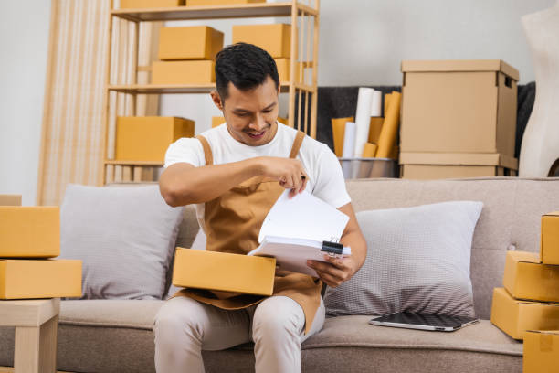 istock Men working from home, managing an online small business, sitting on the sofa, checking items, packing products, and preparing orders for shipment, ensuring timely delivery to customers 2194363129