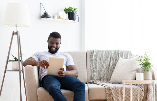 istock Man Sits on Couch Using Tablet in Modern Living Room During Daytime 2194366812