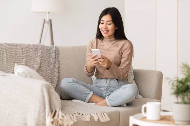 istock Young Woman Sitting on a Couch Using Smartphone in a Modern Living Room Setting 2194367012