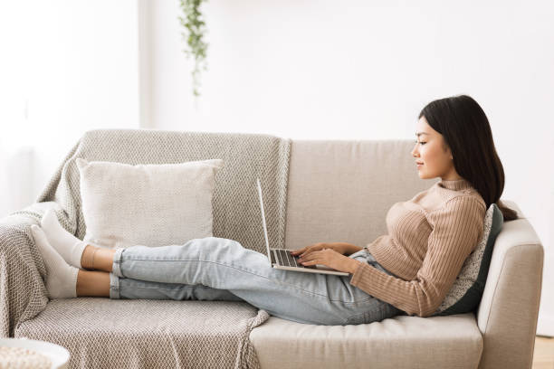 istock Woman Relaxing on Couch While Using Laptop in a Cozy Indoor Setting During Daytime 2194367056