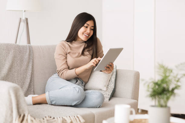 istock Woman Sitting on Couch Using Tablet in Modern Living Room During Daytime 2194367090