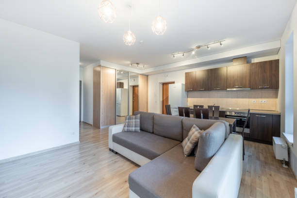istock Modern Home Open Plan Kitchen and Living Room Interior with Dining Table and Window View. A well-lit modern apartment interior featuring an open-plan kitchen, dining area, and cozy living room 2194368295