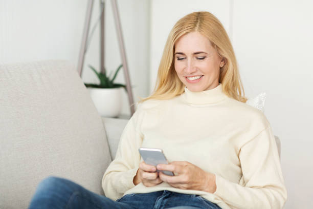 istock Woman Smiling While Using Smartphone at Home in Modern Living Room on a Sunny Day 2194368716