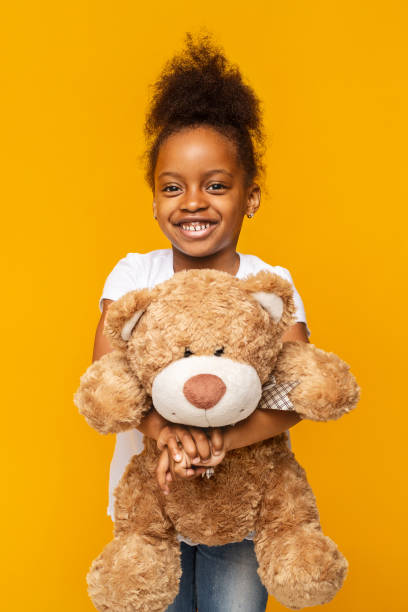istock Young Girl Smiling While Holding a Teddy Bear Against a Bright Yellow Background 2194368968