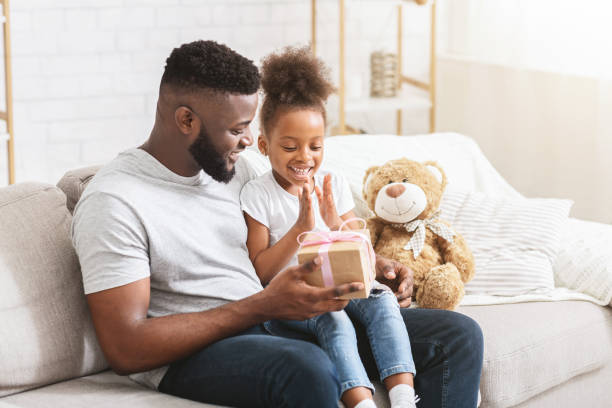 istock Father and Daughter Sharing Joy During Gift Opening at Home on a Cheerful Afternoon 2194369385