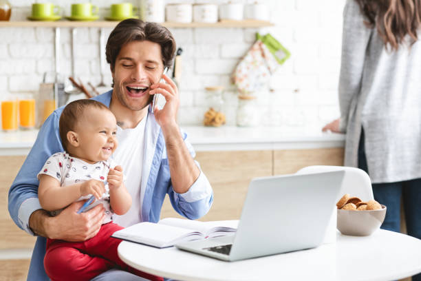 istock Father Happily Spending Time With Baby While on Phone in Modern Kitchen Setting 2194370340
