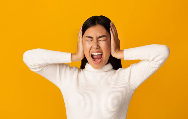 Young Woman Expressing Frustration While Covering Her Ears Against a Bright Yellow Backdrop