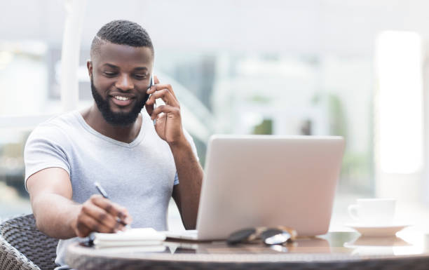 istock Man Working on Laptop While Talking on Phone at Outdoor Cafe During Daytime 2194371988