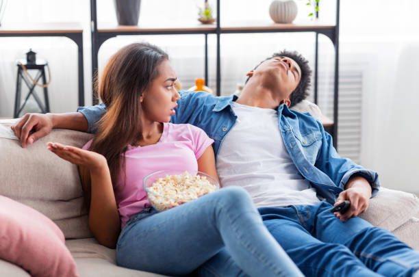 Young Couple Sitting on Sofa With Popcorn During a Disagreement at Home in Daylight