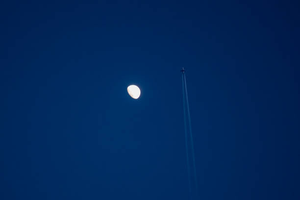 A moon is in the sky above a jet. The sky is clear and blue. The moon is the only object in the sky