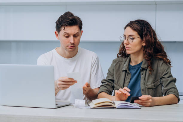 istock Married couple managing finances while discussing bills and budgeting at home using laptop, receipts, and notebook 2194372707