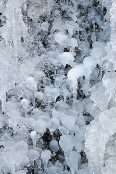 A close-up shot of intricate icicle formations and frozen water droplets creating a captivating winter texture. The scene emphasizes the artistic and natural beauty of ice in a frozen environment.