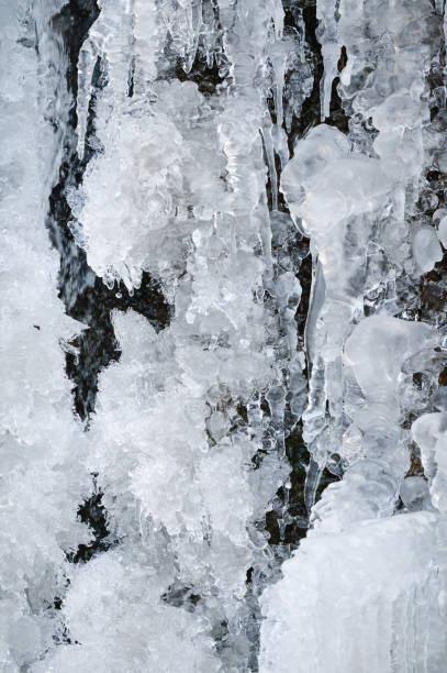 A close-up shot of intricate icicle formations and frozen water droplets creating a captivating winter texture. The scene emphasizes the artistic and natural beauty of ice in a frozen environment.