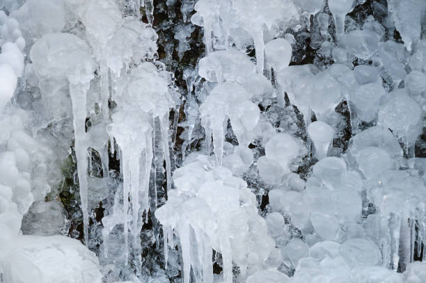 A close-up shot of intricate icicle formations and frozen water droplets creating a captivating winter texture. The scene emphasizes the artistic and natural beauty of ice in a frozen environment.