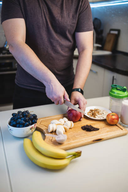 istock Man preparing a protein drink in a kitchen, cutting an apple on a table with bananas, walnuts, and grapes, in the kitchen 2194379354